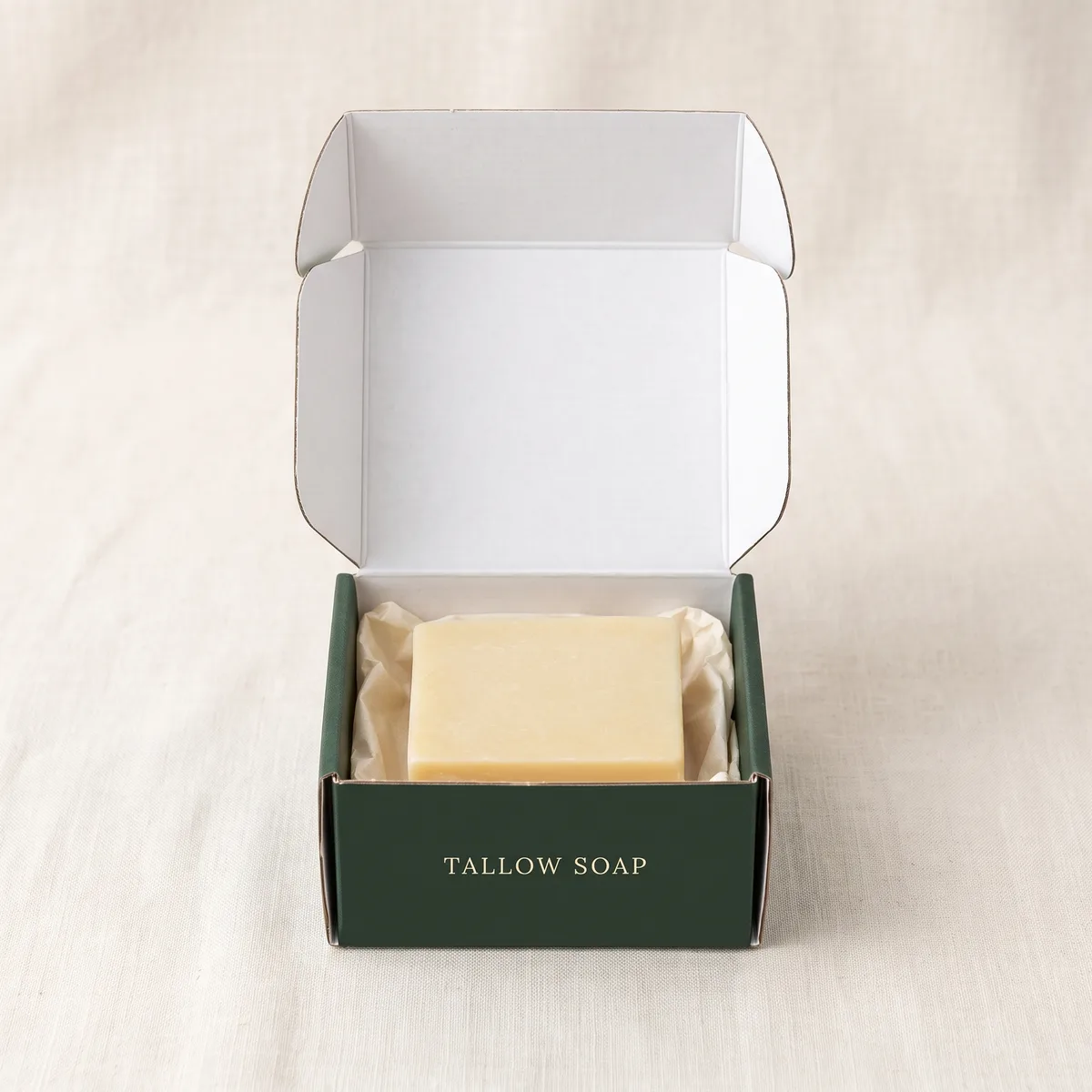 Open custom soap box with a bar of tallow soap resting on tissue paper inside