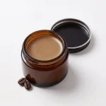 Coffee & Tallow Eye Balm in an open amber glass jar with coffee beans